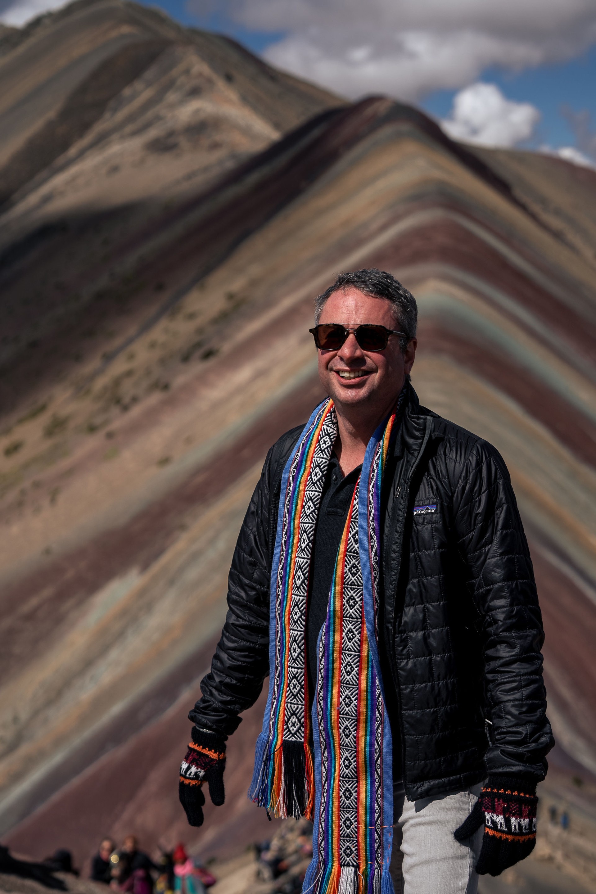 Shaun Southworth smiling at Rainbow Mountain in Peru, wearing a colorful woven scarf and cold-weather jacket
