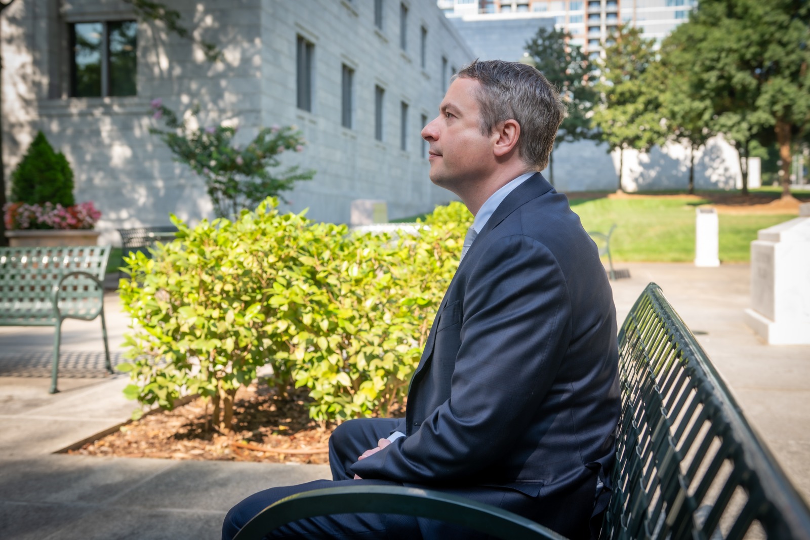 Shaun Southworth seated on a garden bench, looking across a tree-lined courtyard